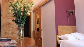 Una habitación de hotel con cabecera de madera, lámpara de noche, cama con ropa blanca y un jarrón con flores sobre una mesa de madera.