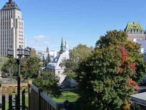 A view of a cityscape with a prominent building with vertical lines, a church with a green roof, and a tree with autumn leaves. - Castel d'Amérique Française (Québec City)