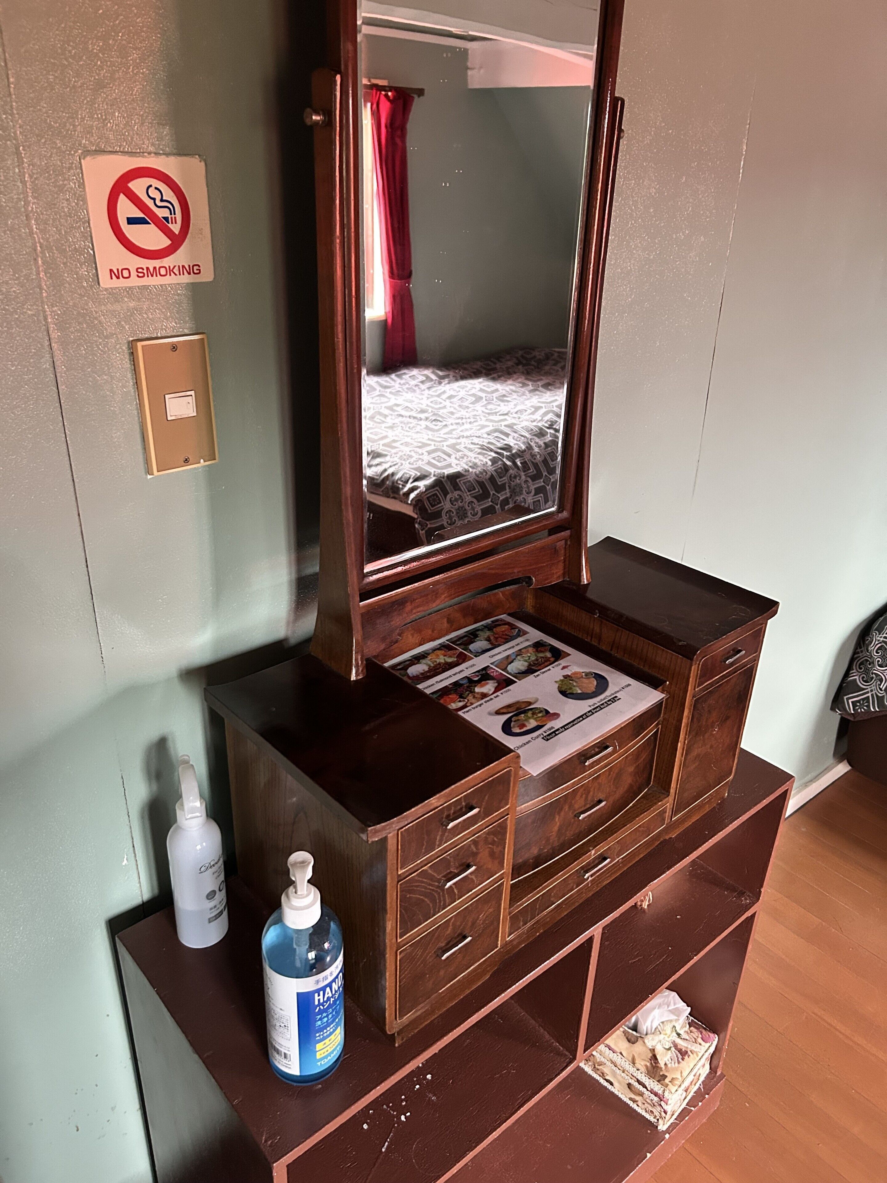 Een houten dressoir met een spiegel, een 'NO SMOKING' bordje, een lichtschakelaar en een menukaart op de spiegel.
