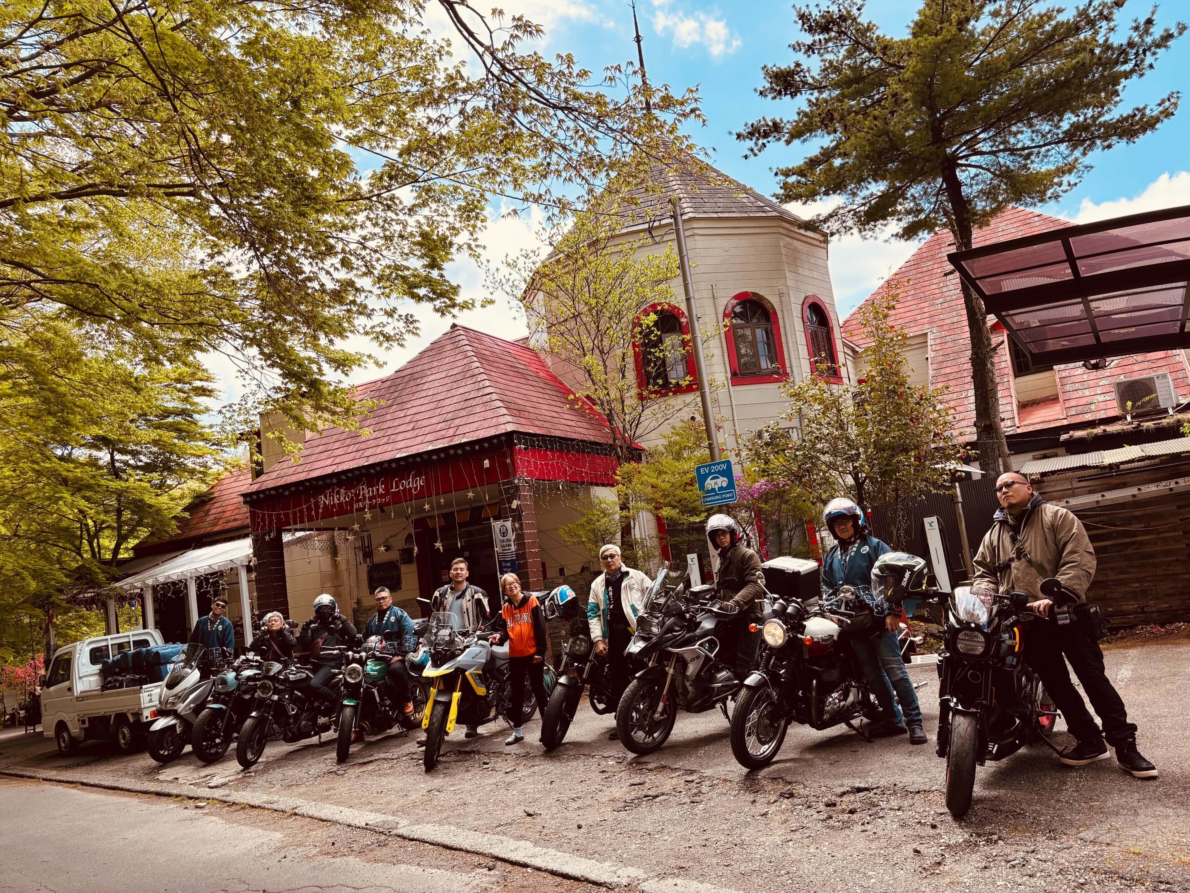 Eine Gruppe von Personen mit Motorrädern vor einem Gebäude mit rotem Dach und einem Schild mit der Aufschrift 'Nikola Park Lodge'.