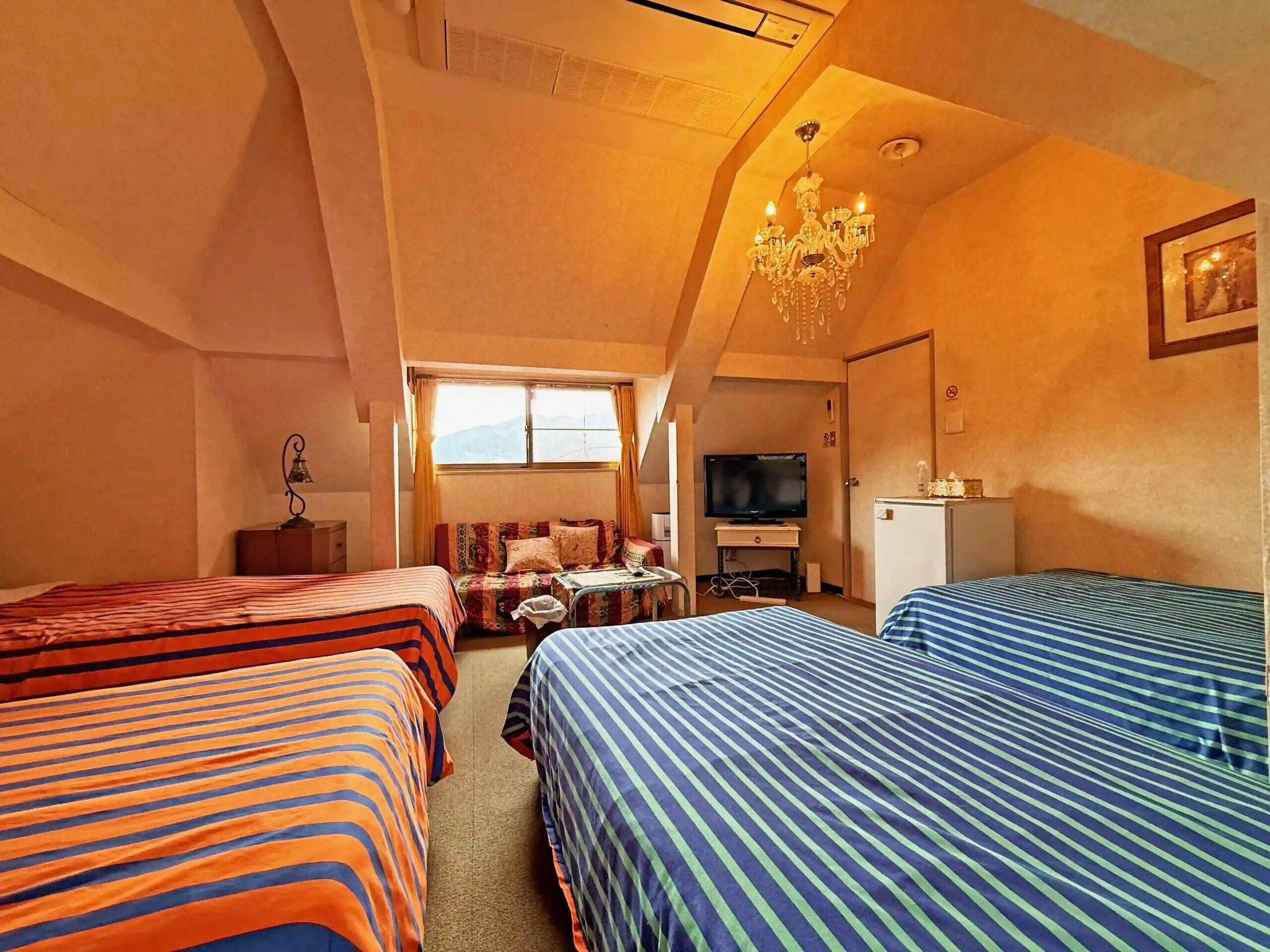 A room with two beds, a television, a small table, and a chandelier.