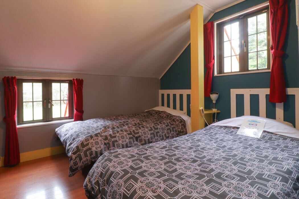 Un dormitorio con dos camas, una ventana con cortinas y un cabecero blanco.