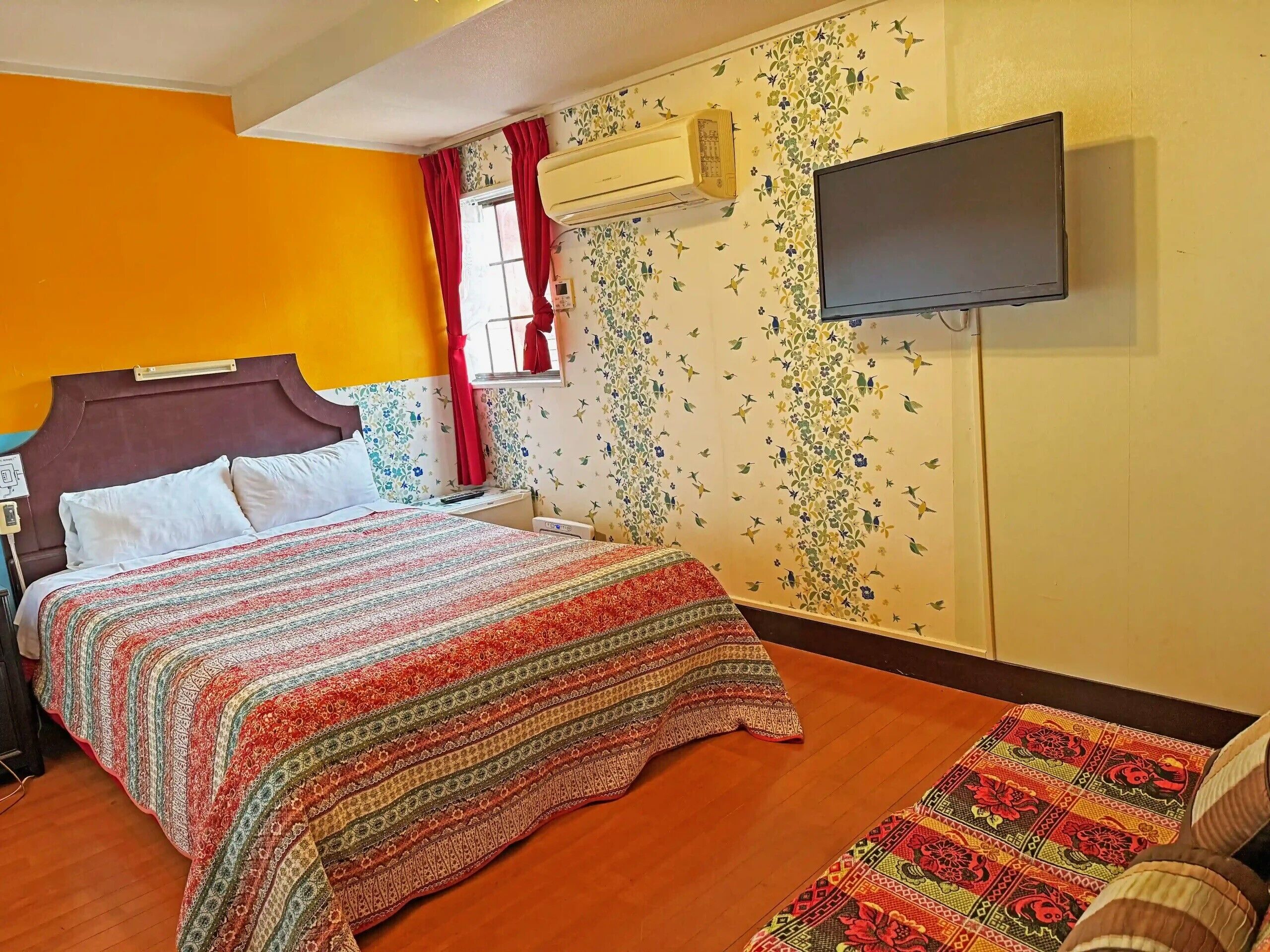 Habitación de hotel con cama, televisión, ventana con cortinas y un papel tapiz floral.