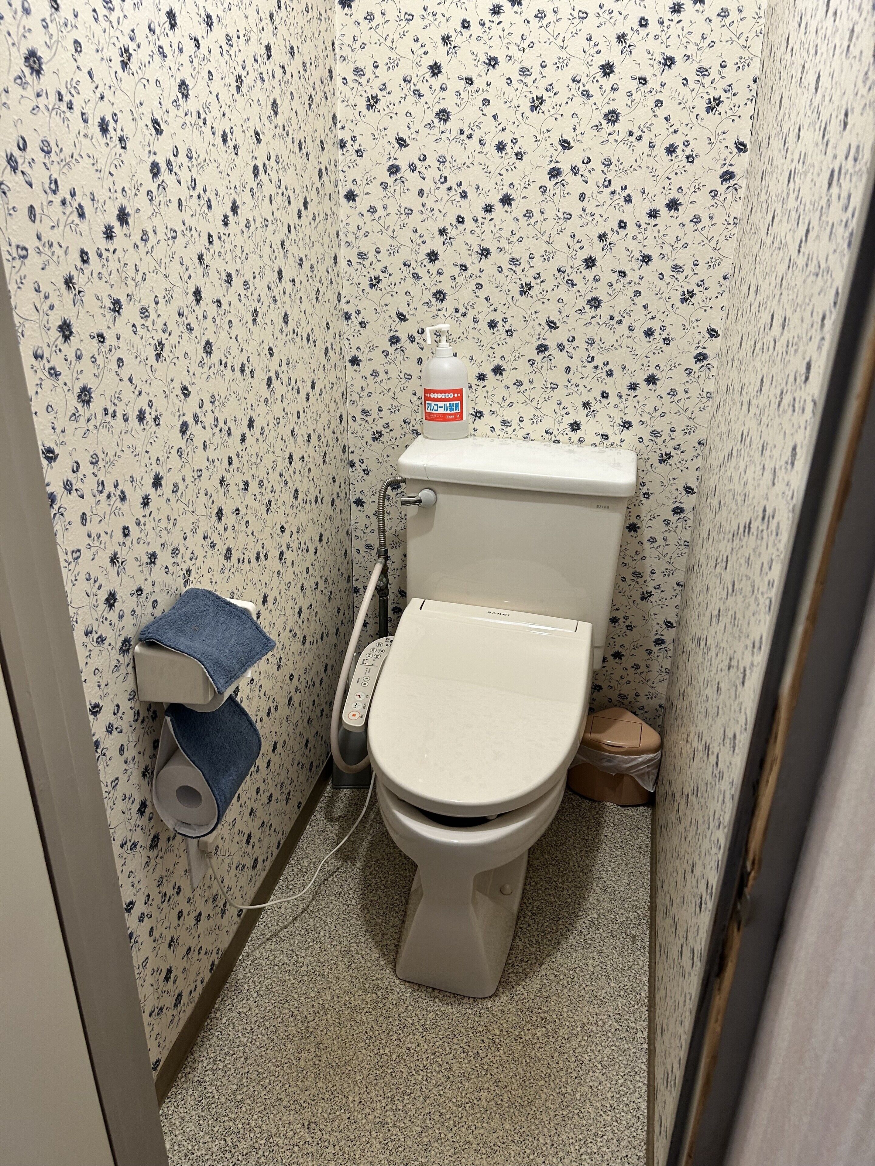 Un baño pequeño con inodoro, dispensador de toallas de papel y rollo de papel higiénico.
