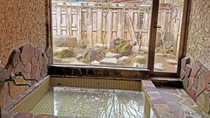 A stone bathtub with a tiled floor, a wooden fence, and a view of a garden. - Nikko Park Lodge Mountainside (Nikko)