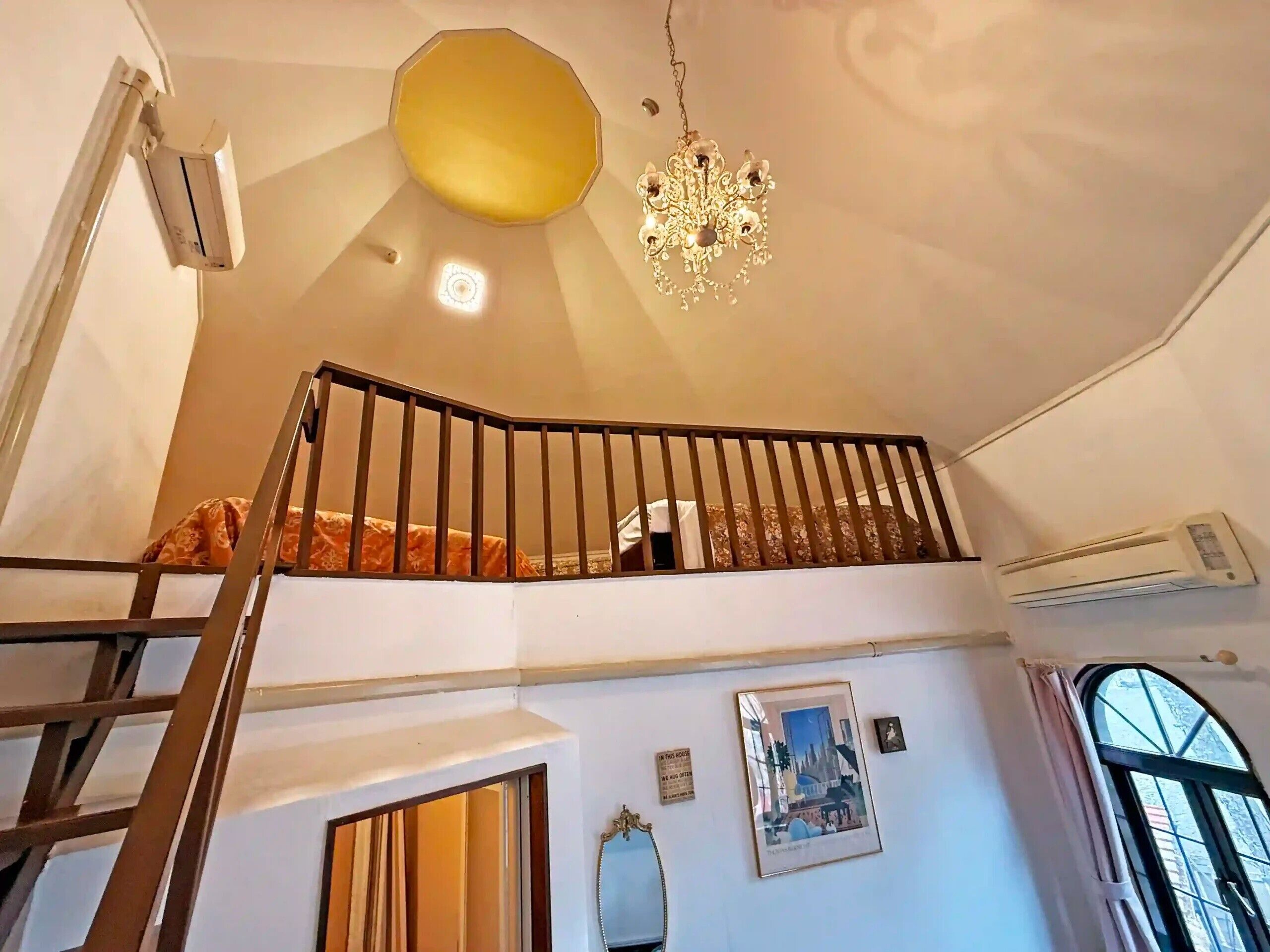 A staircase with a black railing, a chandelier, and an air conditioning unit on the wall.