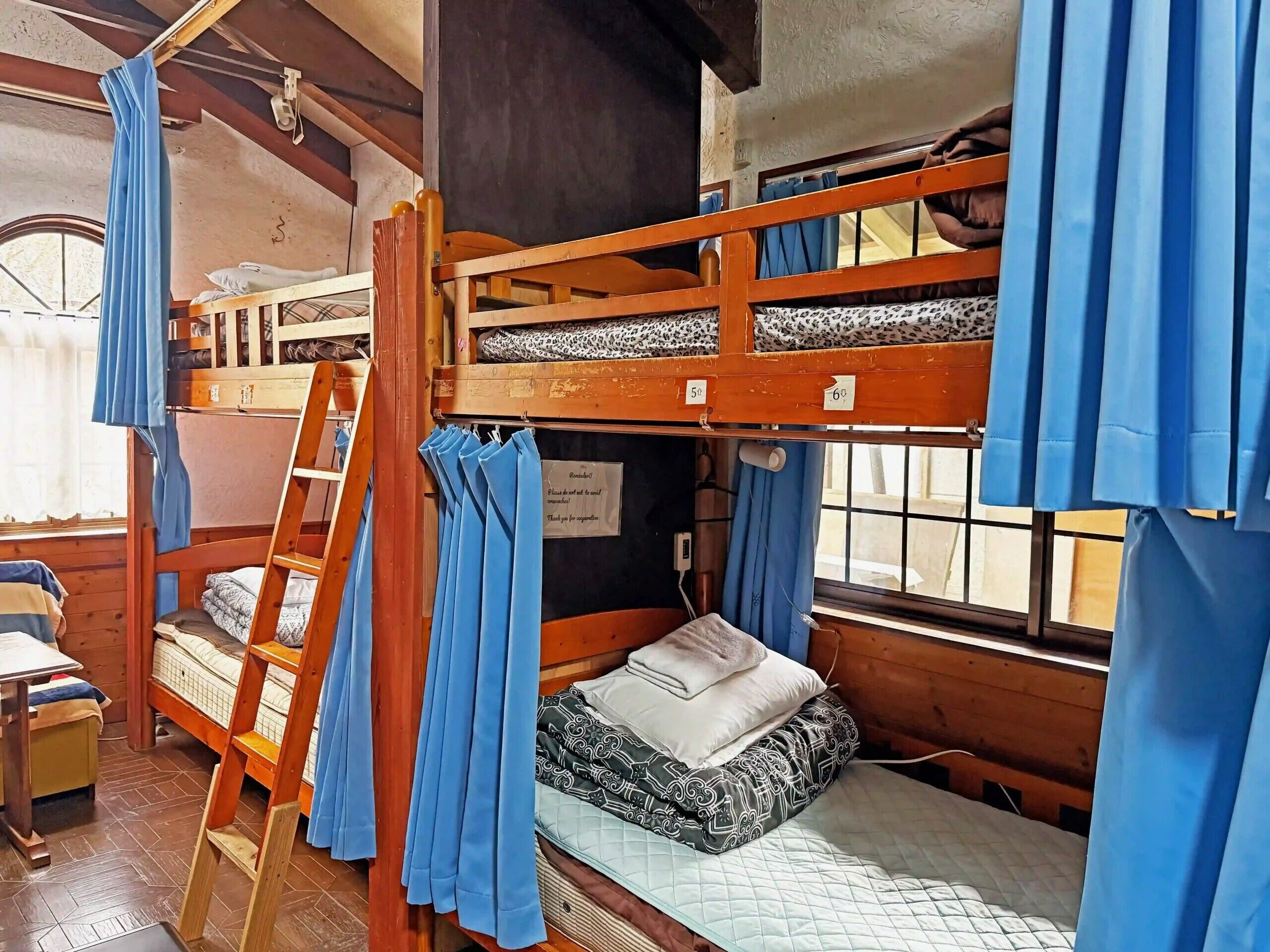 A bunk bed room with a ladder, a window with curtains, and a bed with a quilted mattress.