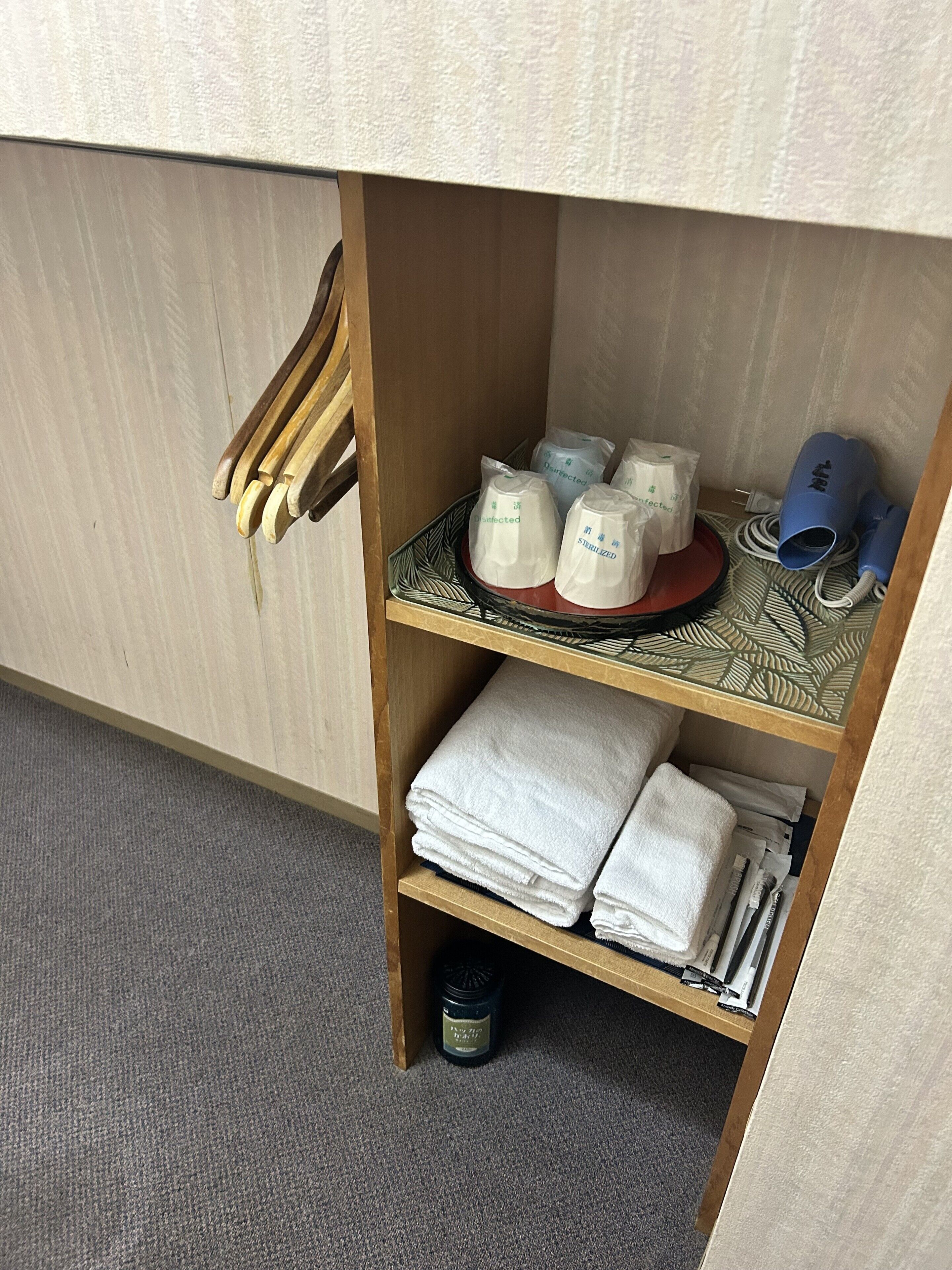 A wooden shelf with neatly folded white towels, disinfected and sterilized bags, a blue hairdryer, and a black container.