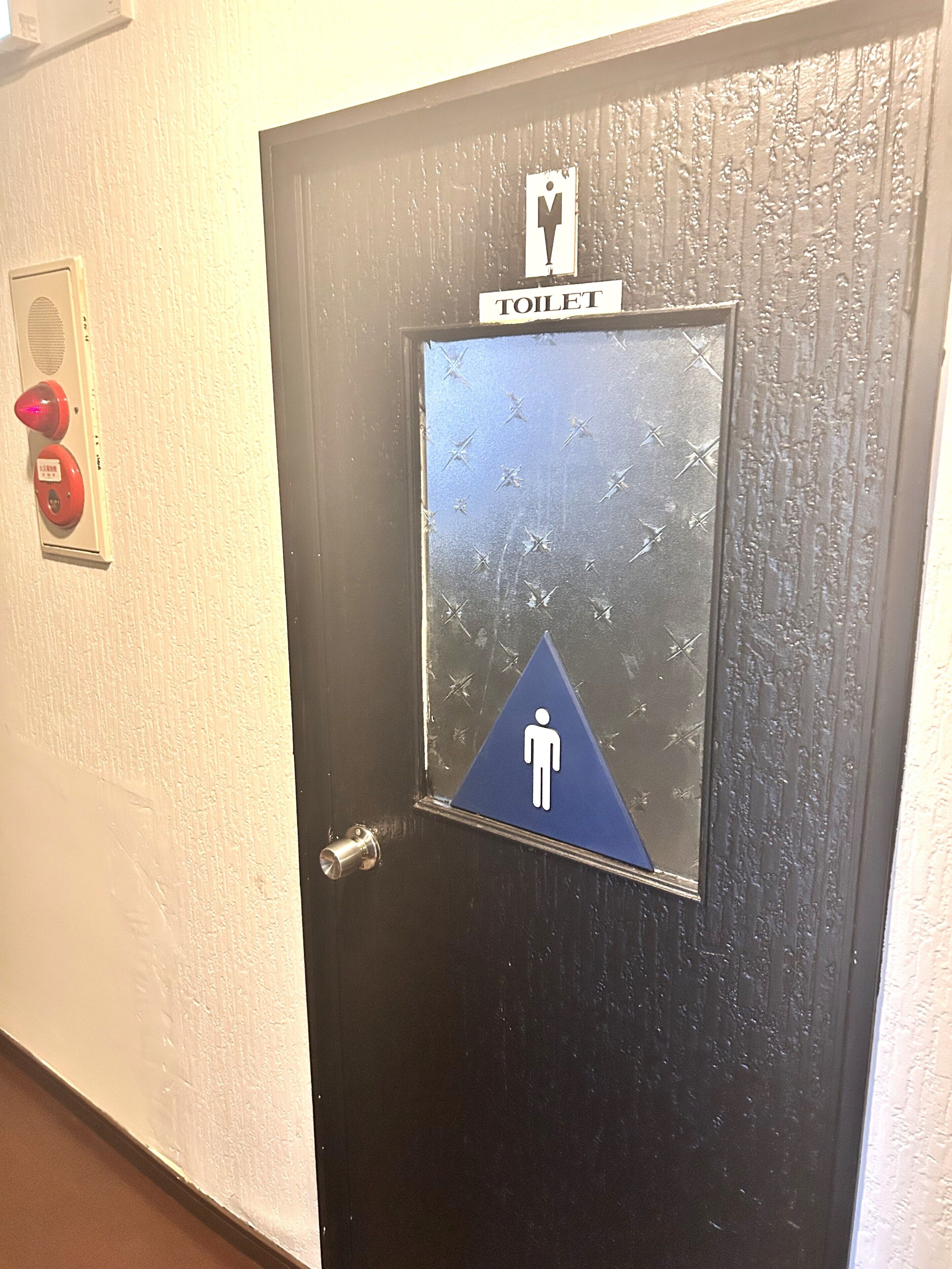 A door with a peephole, a peephole sign, and a fire alarm button.
