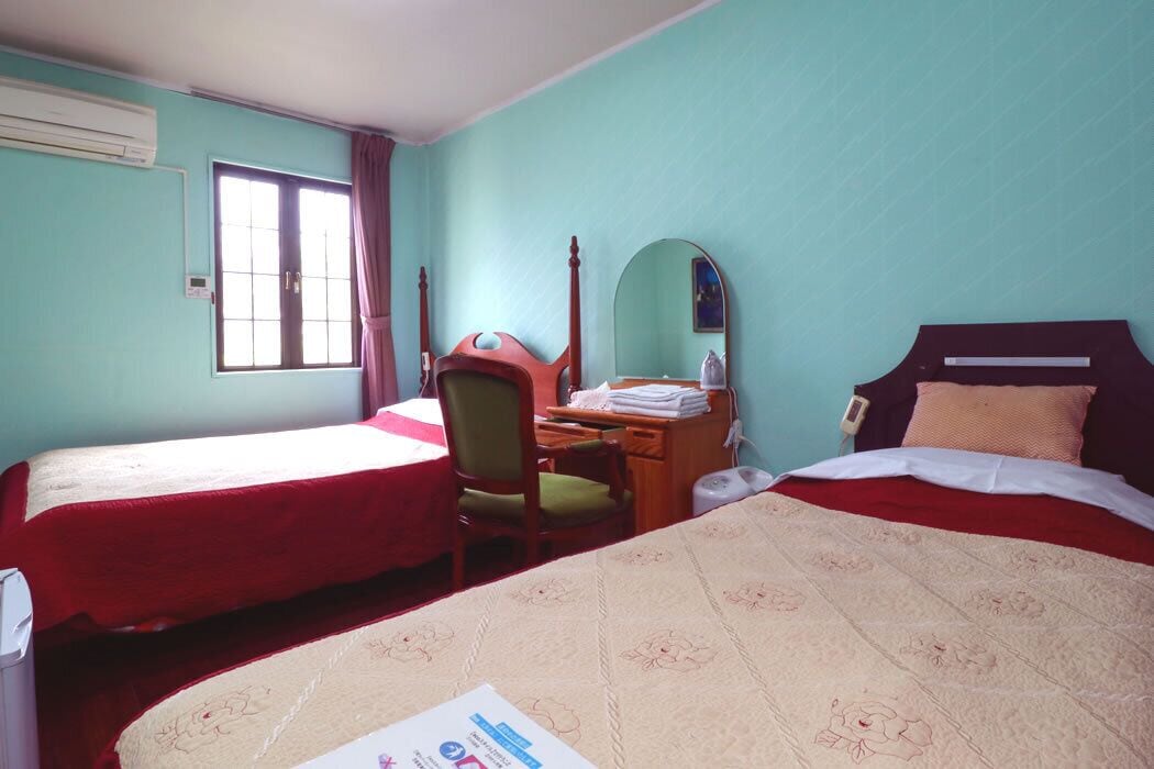 A hotel room with two beds, a desk, a chair, a mirror, and a window.