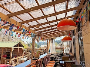 Un espace extérieur aménagé dans un style rustique, avec des tables et des chaises en bois, un barbecue et une vue sur les montagnes.