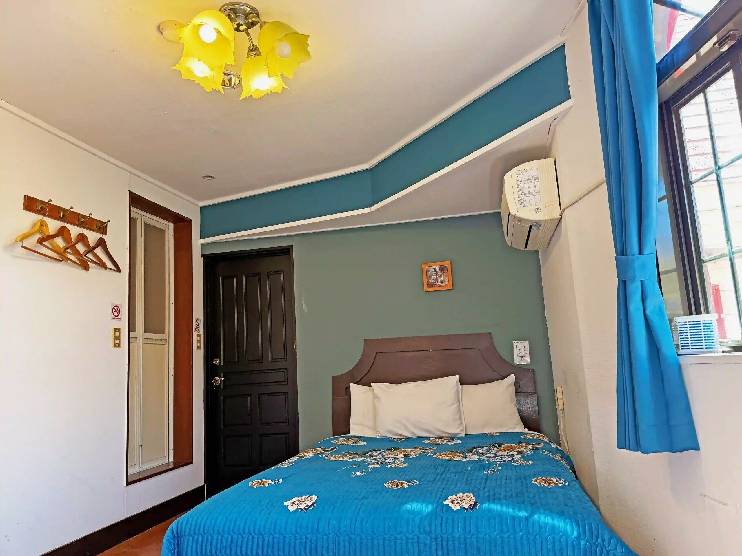 Ein Schlafzimmer mit Bett, Deckenleuchte, Tür und einem Fenster mit Vorhängen.