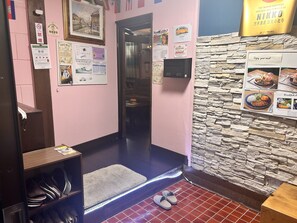 A hotel room with a stone wall, a wooden shelf with slippers, a door leading to a bathroom, and various informational posters on the walls. - Nikko Park Lodge Mountainside (Nikko)