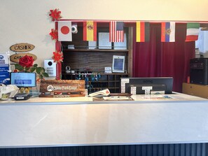 Un comptoir d’accueil avec une pancarte indiquant « CAISSE », un ordinateur, une horloge et divers drapeaux.