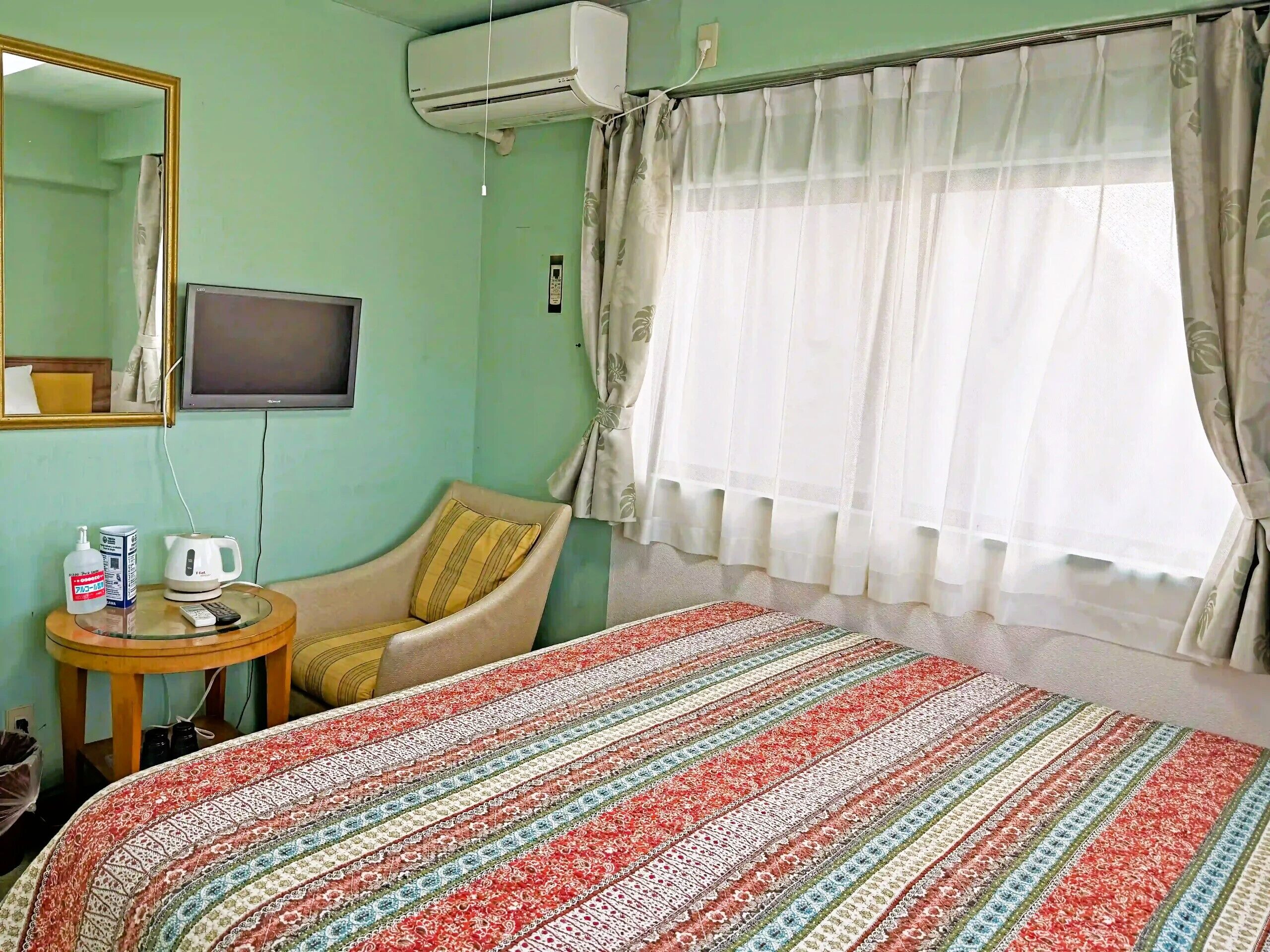 A room with a bed, a chair, a television, and a window with curtains.
