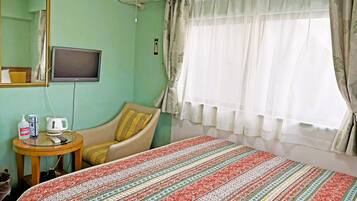 A room with a bed, a chair, a television, and a window with curtains.