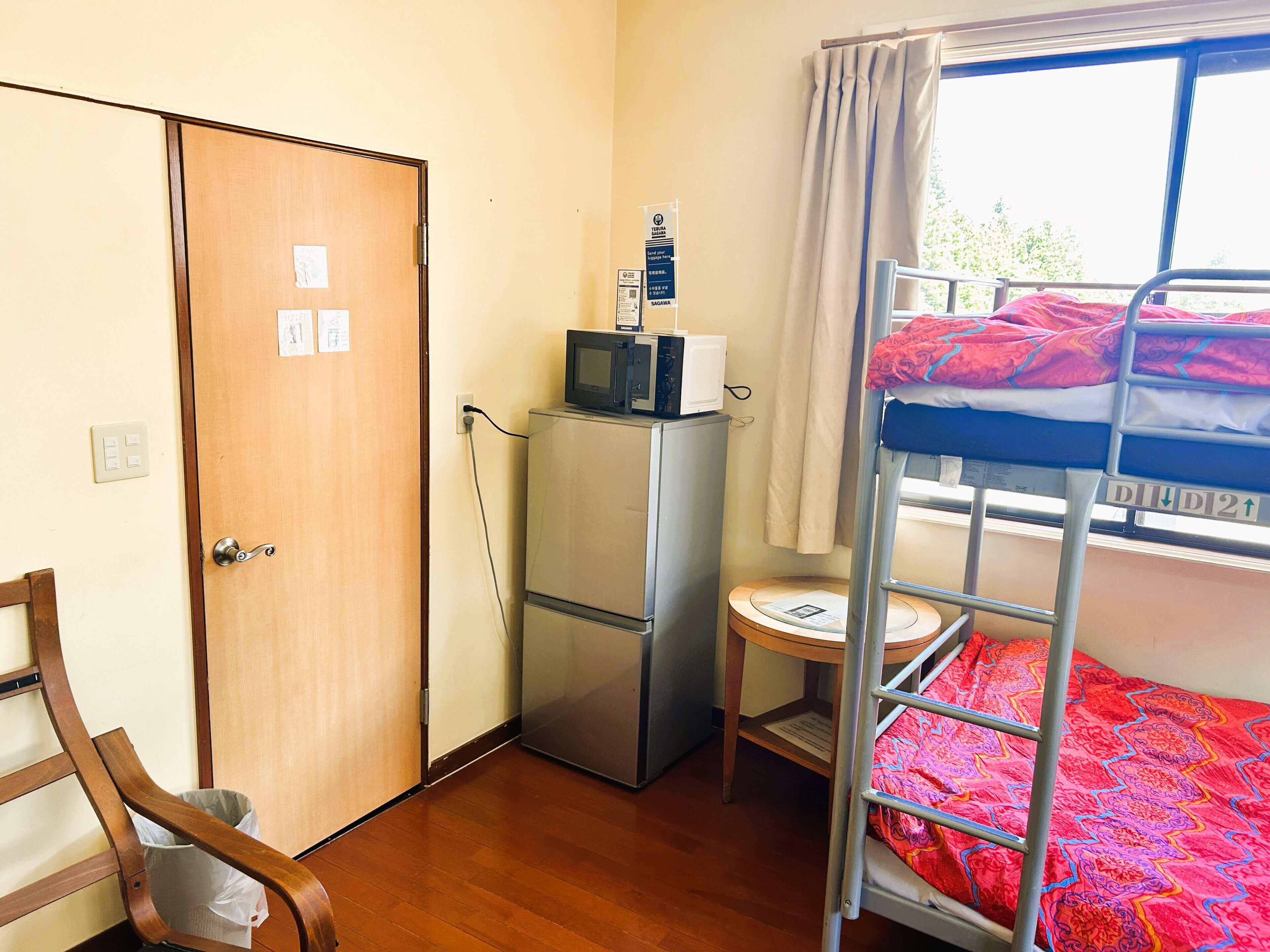 A compact room with a bunk bed, a refrigerator, a microwave, a small table, and a door with a light switch.