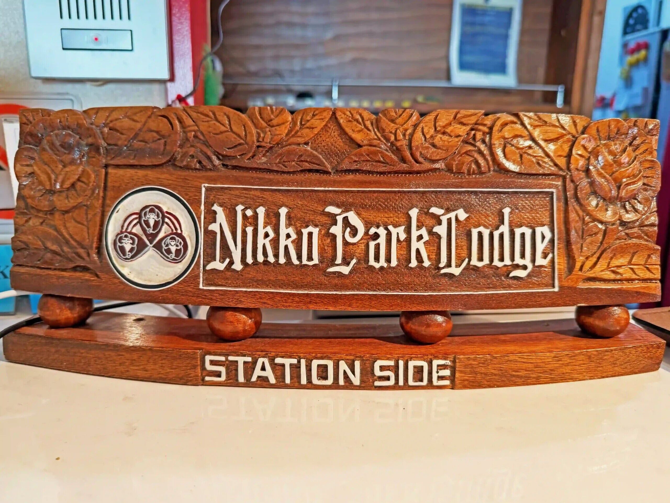 Un letrero de madera con el texto 'Nikko Park Lodge' y 'Station Side', rodeado de diseños de hojas talladas.