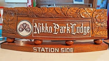 Un letrero de madera con el texto 'Nikko Park Lodge' y 'Station Side', rodeado de diseños de hojas talladas.