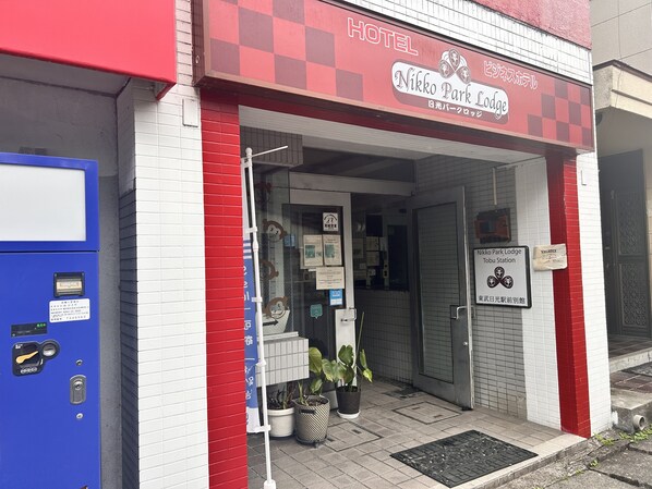 A hotel entrance with a red and white facade, a blue vending machine, and a sign indicating a vacancy. - Nikko Park Lodge Tobu Station (Nikko)