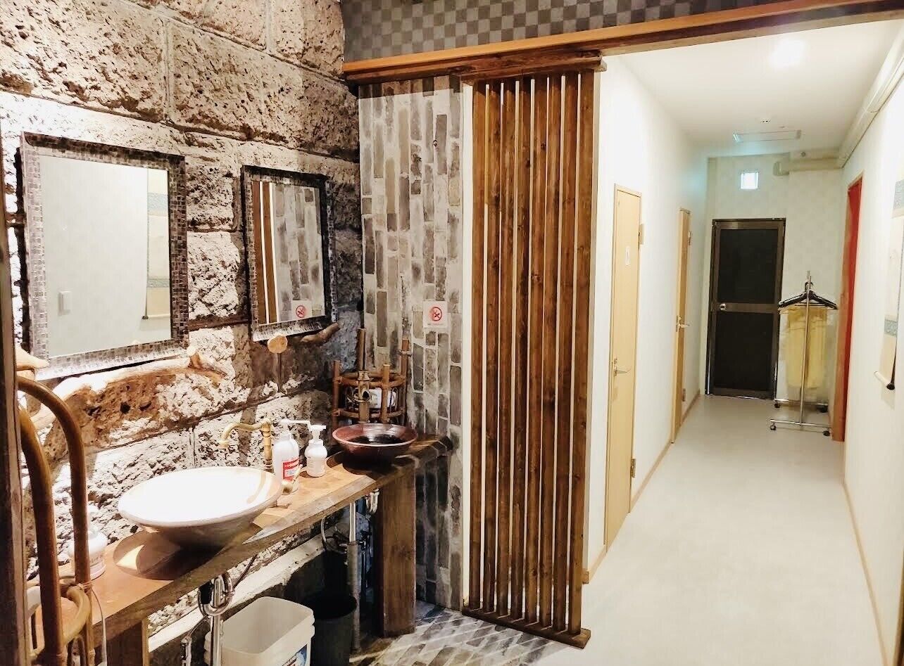 A bathroom with a stone wall, a wooden vanity, a sink, a mirror, and a shower area.