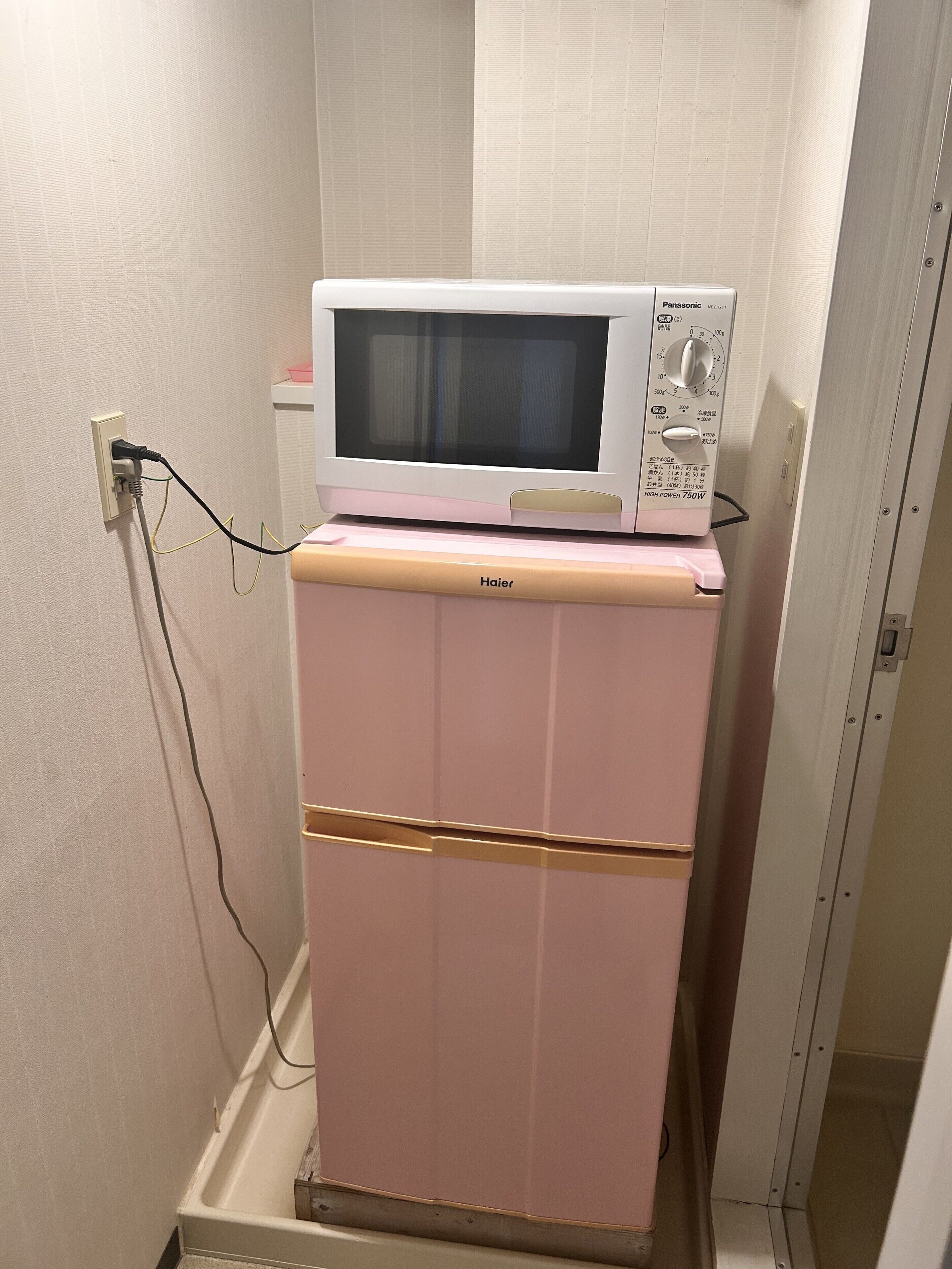 A pink Haier refrigerator with a microwave on top, connected to a power outlet.