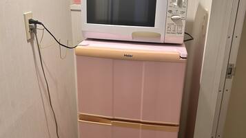 A pink Haier refrigerator with a microwave on top, connected to a power outlet.