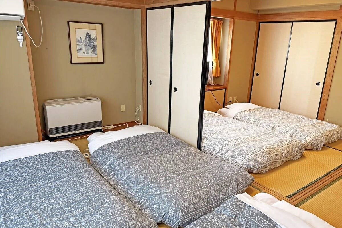 A traditional Japanese room with tatami flooring, a bed with patterned bedding, a heater, and a sliding door.
