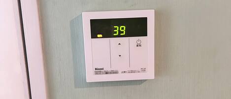 Interruptor de agua caliente con pantalla digital que indica 39 grados Celsius, panel de control y un interruptor de luz estándar debajo.