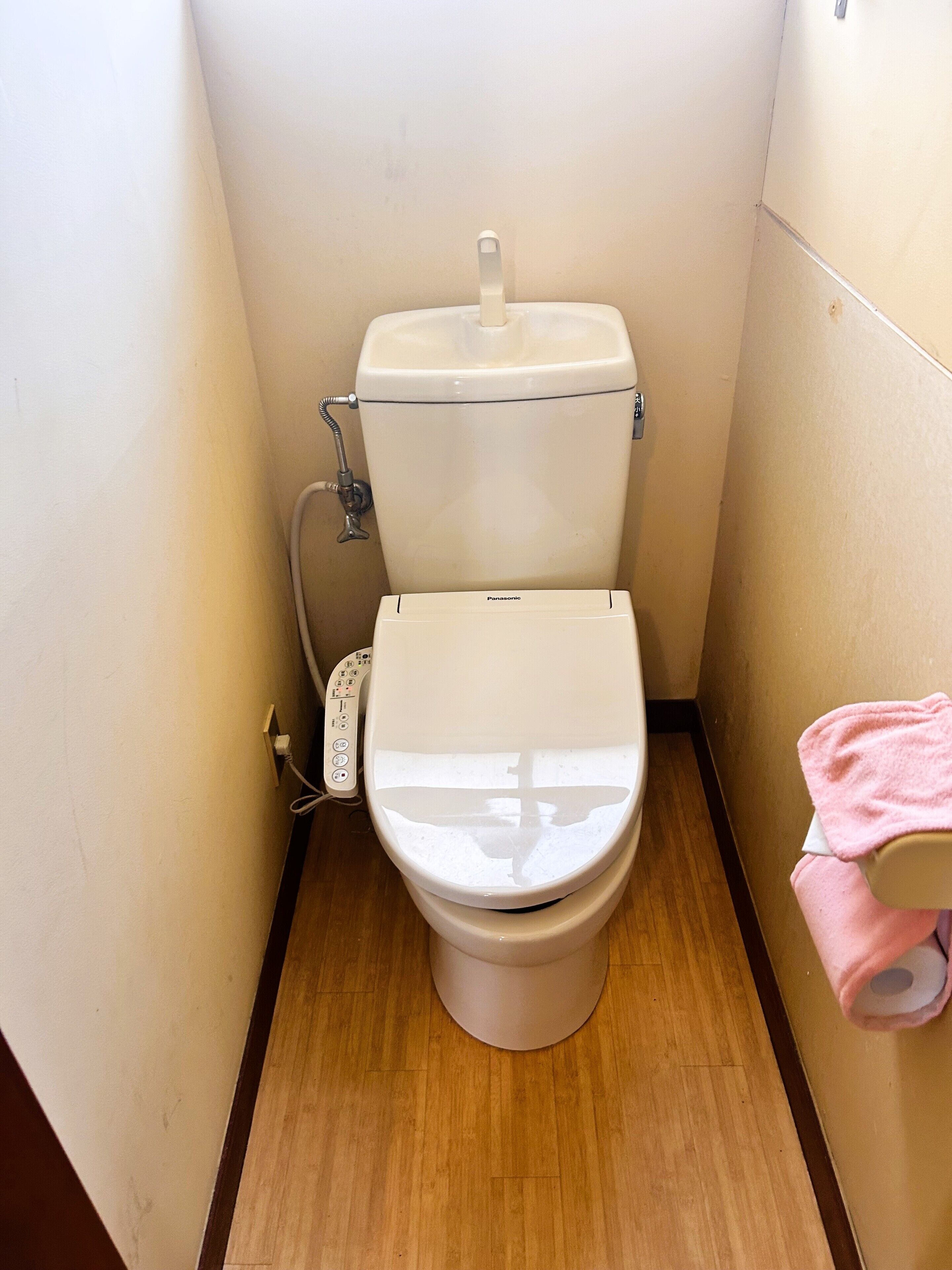 A toilet with a control panel, a pink towel, and a roll of toilet paper.