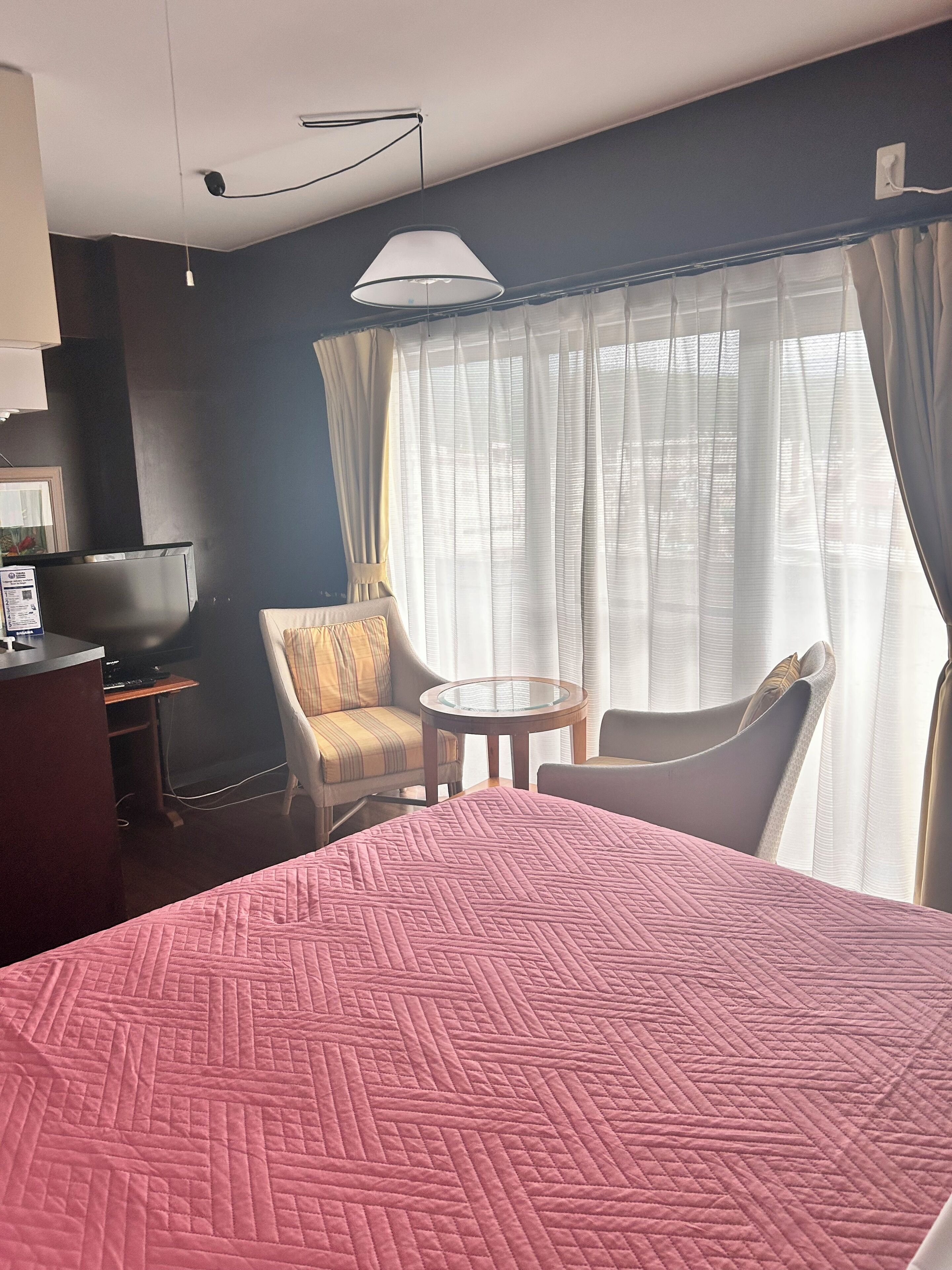 Ein Hotelzimmer mit Bett, Schreibtisch, Stuhl und einem Vorhangfenster.