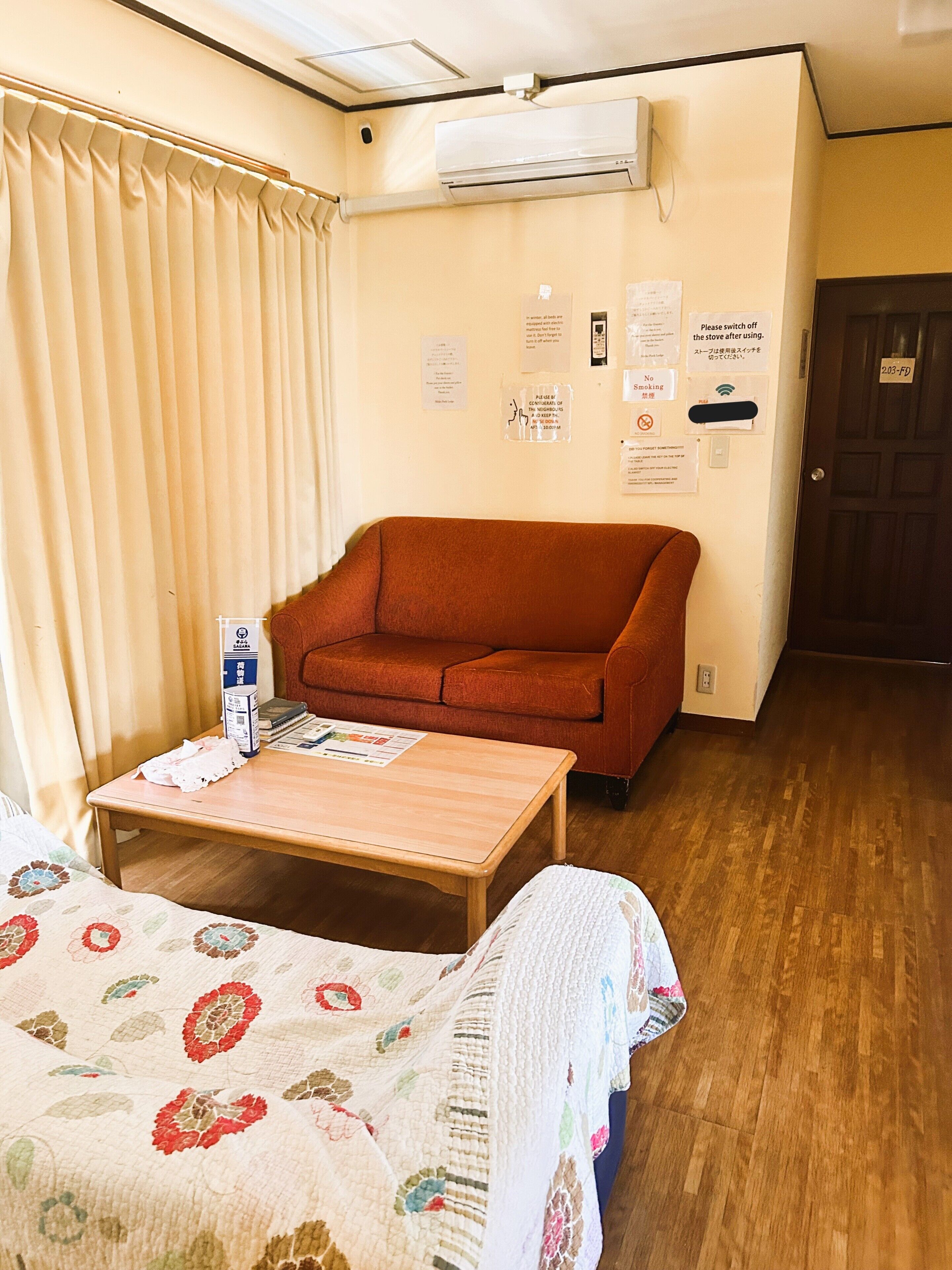 Una habitación con suelo de madera, un sofá rojo, una mesa de madera y una cama con colcha estampada.