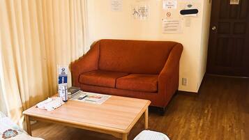 Una habitación con suelo de madera, un sofá rojo, una mesa de madera y una cama con colcha estampada.