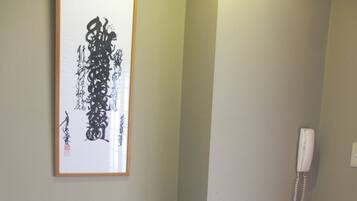 Ein Zimmer mit einem gerahmten Kalligraphie-Kunstwerk, einer traditionellen japanischen Puppenausstellung, einem kleinen Tisch und einem Telefon an der Wand.