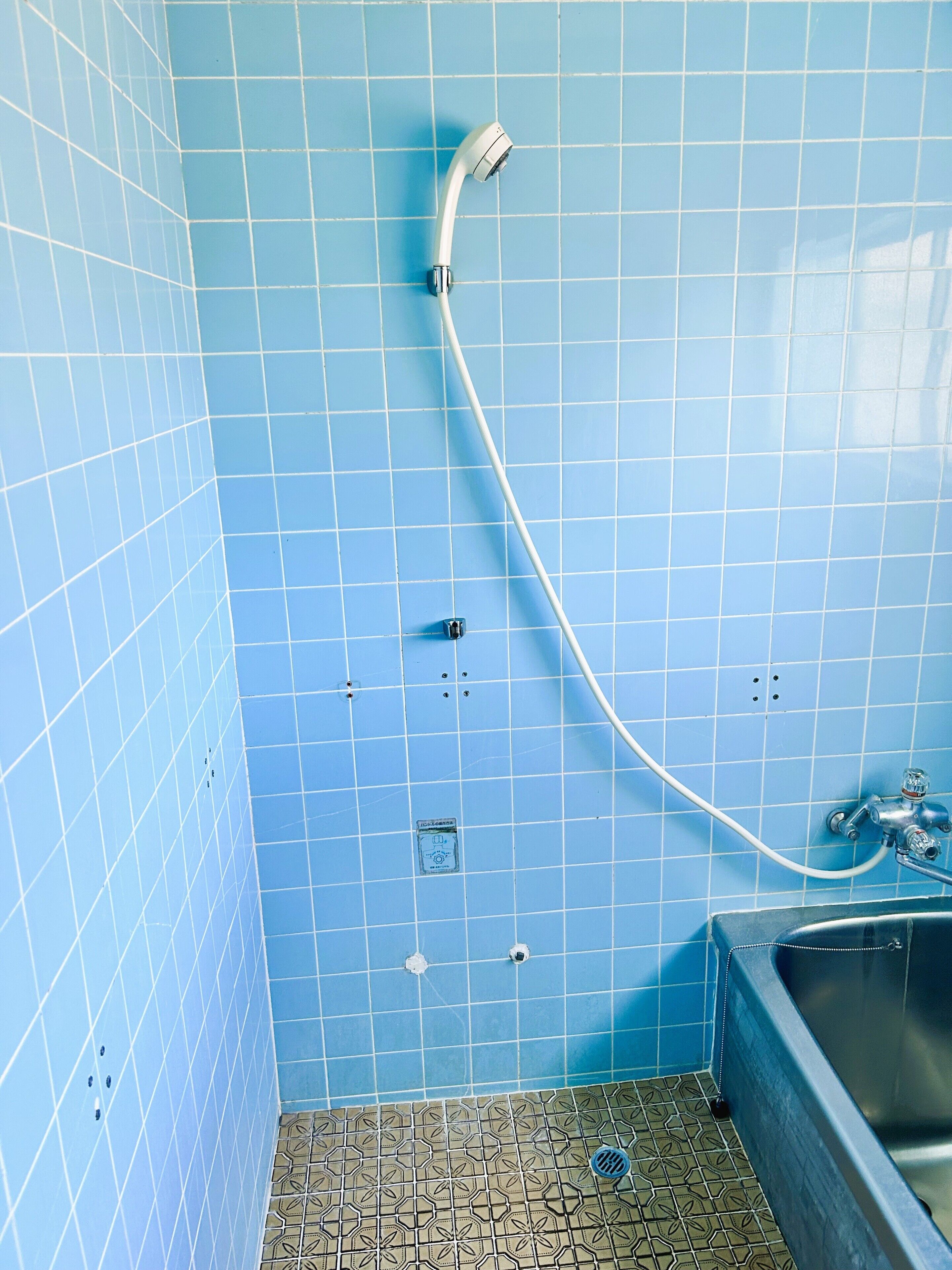 A bathroom with blue tiled walls, a shower, and a sink.