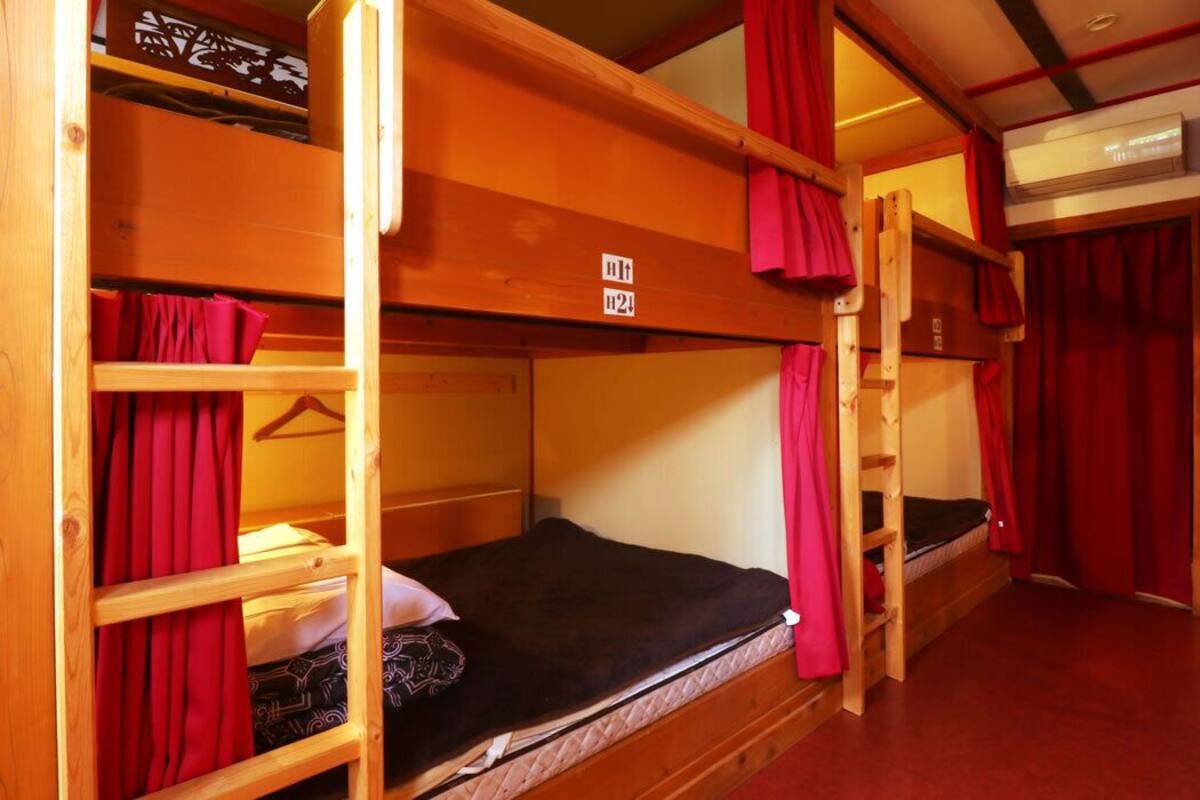 A bunk bed room with wooden railings, red curtains, and a visible air conditioning unit.