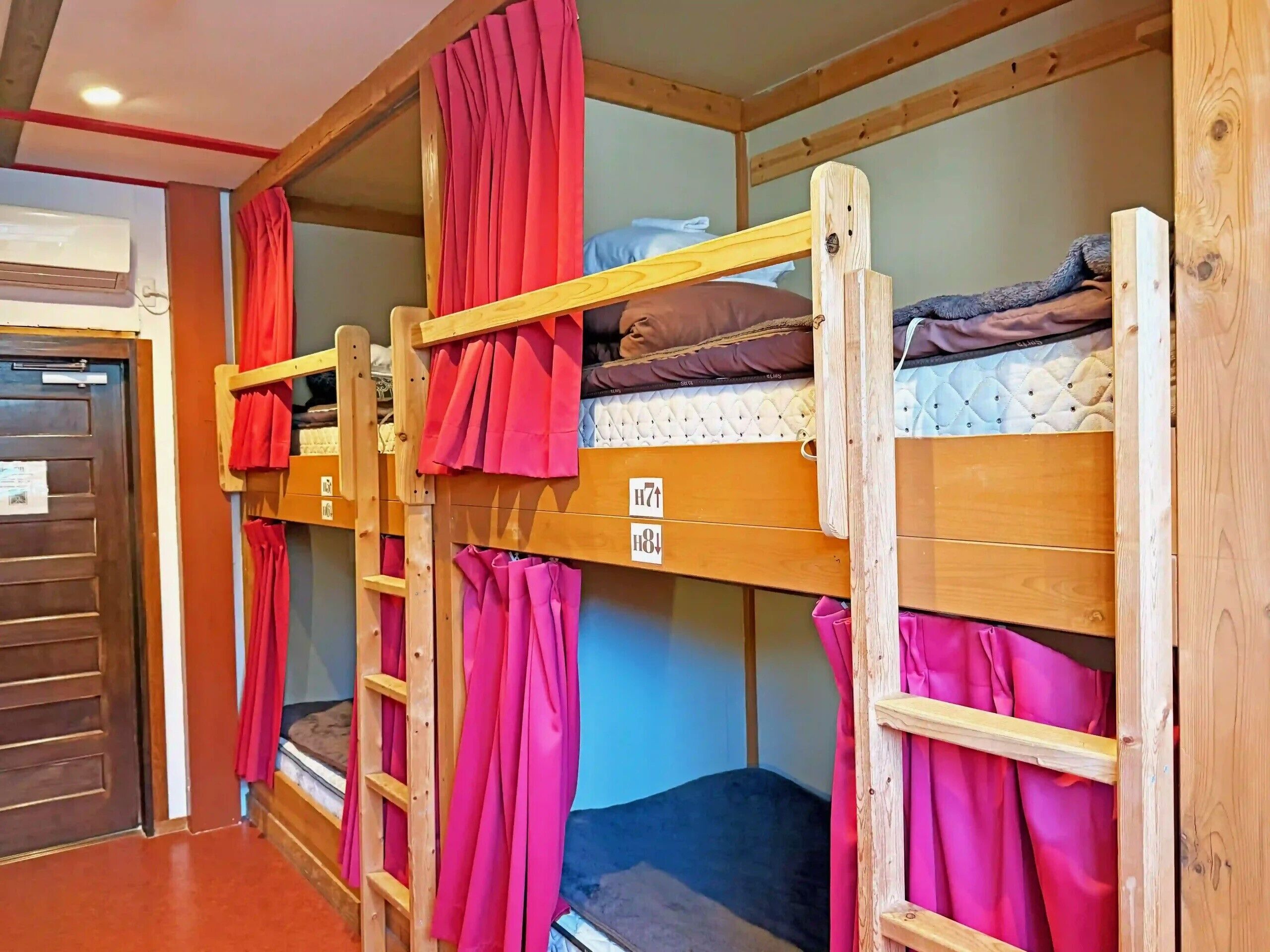 Bunk beds with curtains, a wooden door, and a wall-mounted air conditioner.