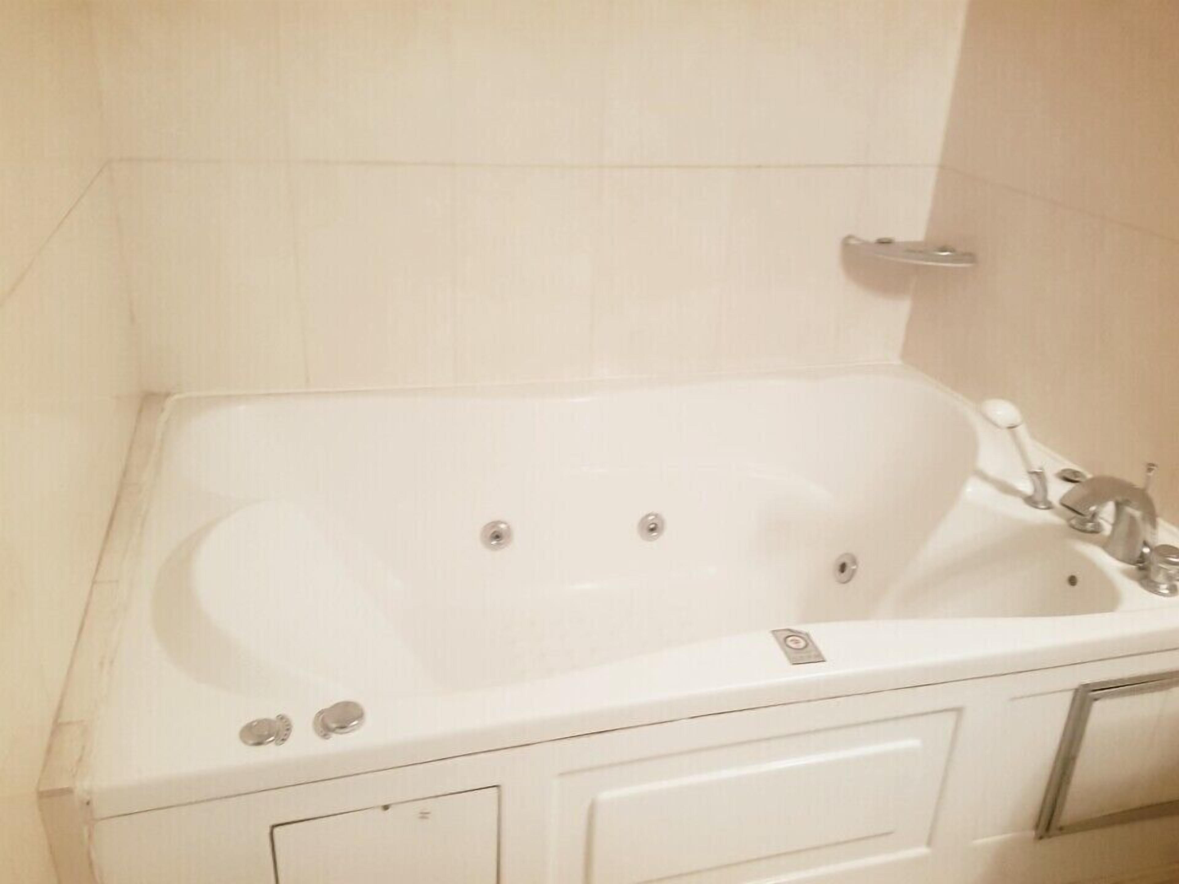Una bañera blanca con un solo grifo y una llave mezcladora, ubicada en un baño con azulejos blancos.