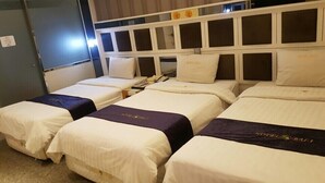 Una camera d'albergo con quattro letti disposti in fila, ognuno con biancheria bianca e un tocco di colore viola.