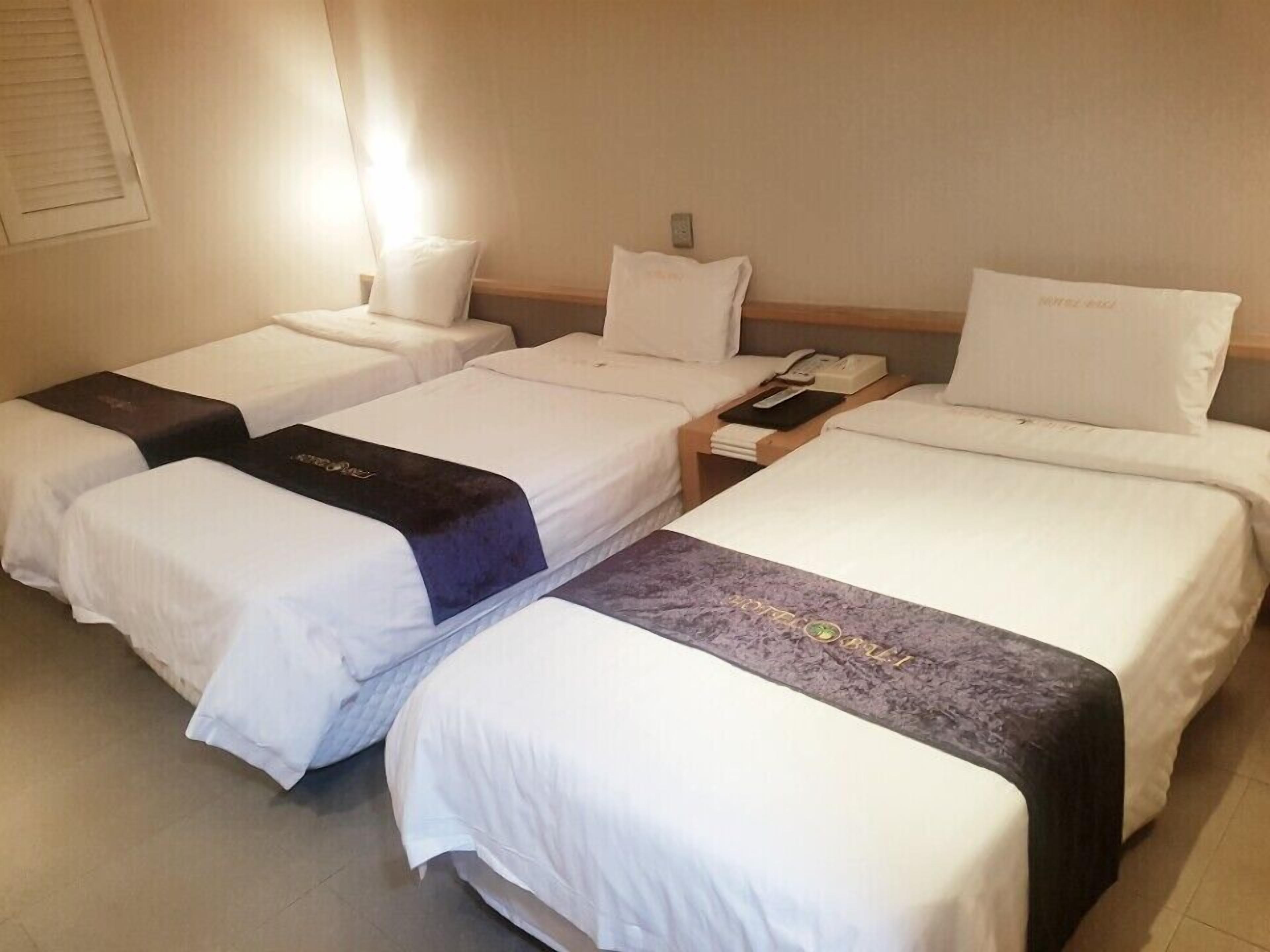 Quarto de hotel com três camas de solteiro, cada uma com travesseiro e mesa de cabeceira.