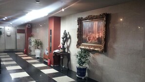 Una hall con pavimento a scacchi, una statua, un quadro incorniciato e piante in vaso.