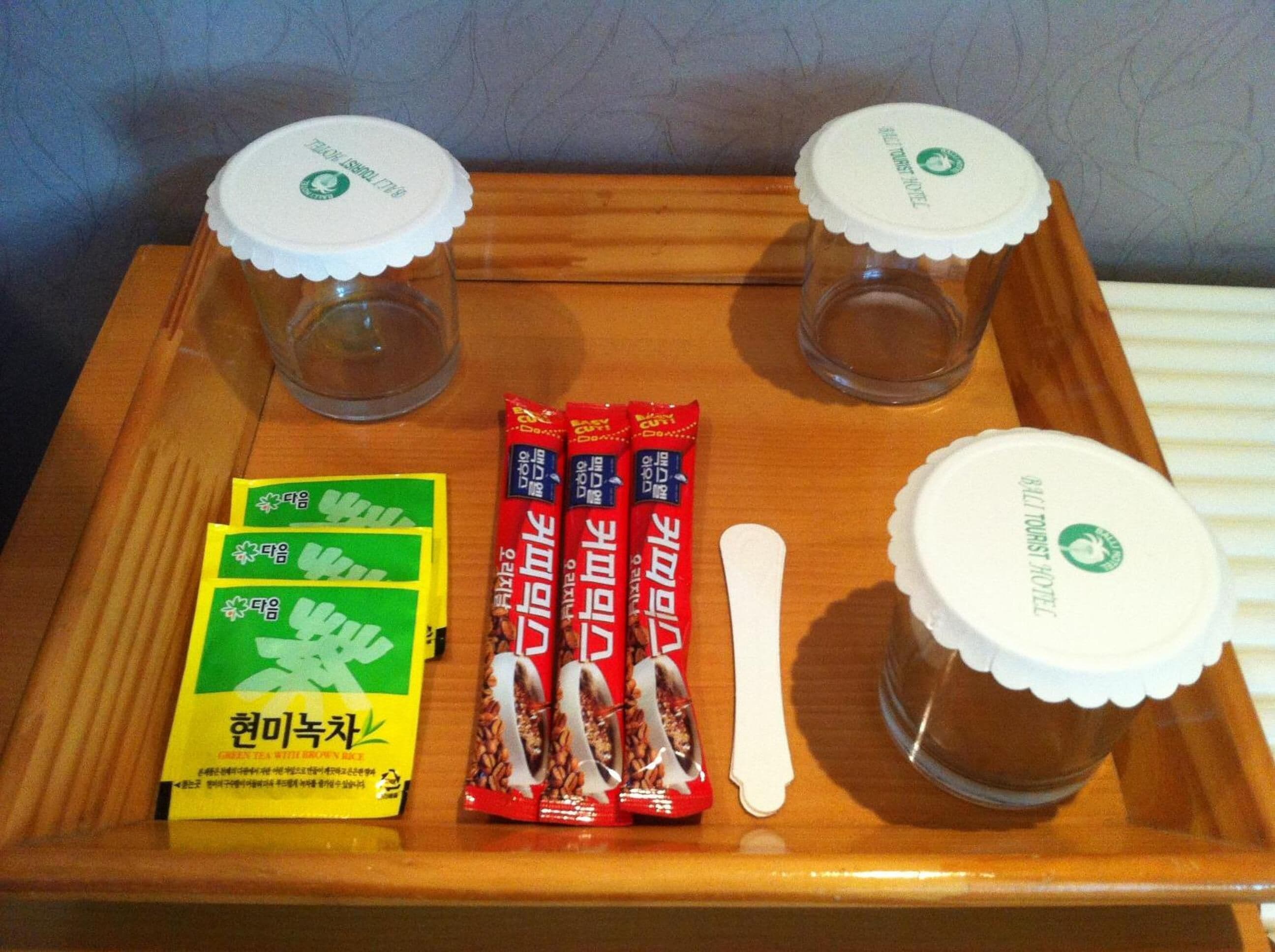 Una bandeja de madera con dos tazas de vidrio pequeñas, dos sobres de comida roja, un sobre de té verde y una cuchara blanca.