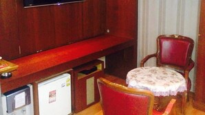 Un ambiente compatto con TV a schermo piatto fissata a una parete in legno, un piccolo frigorifero, un tavolo da pranzo con due sedie e una tenda a righe.