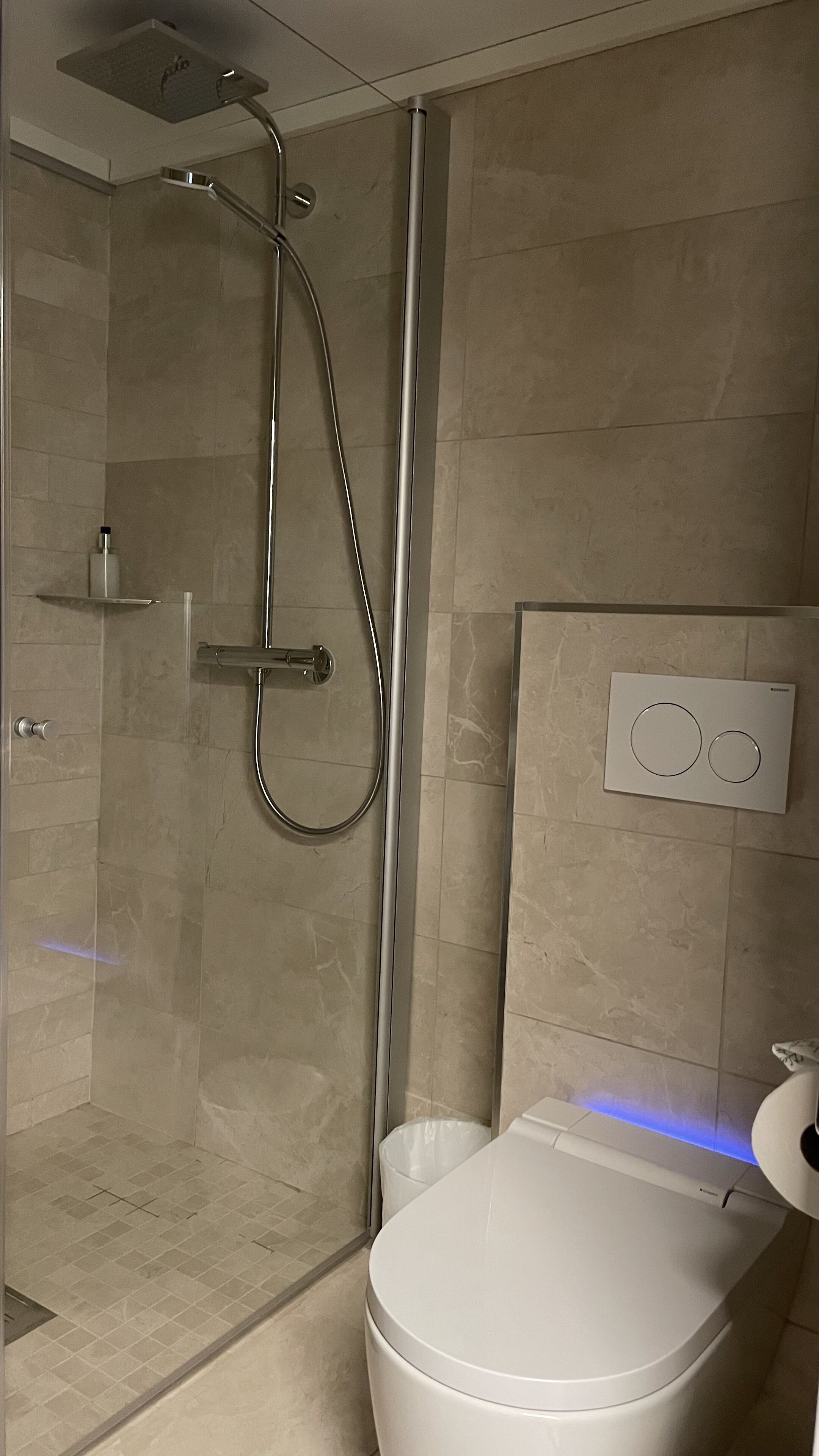 A modern bathroom with a glass-enclosed shower, a toilet, and a wall-mounted control panel.