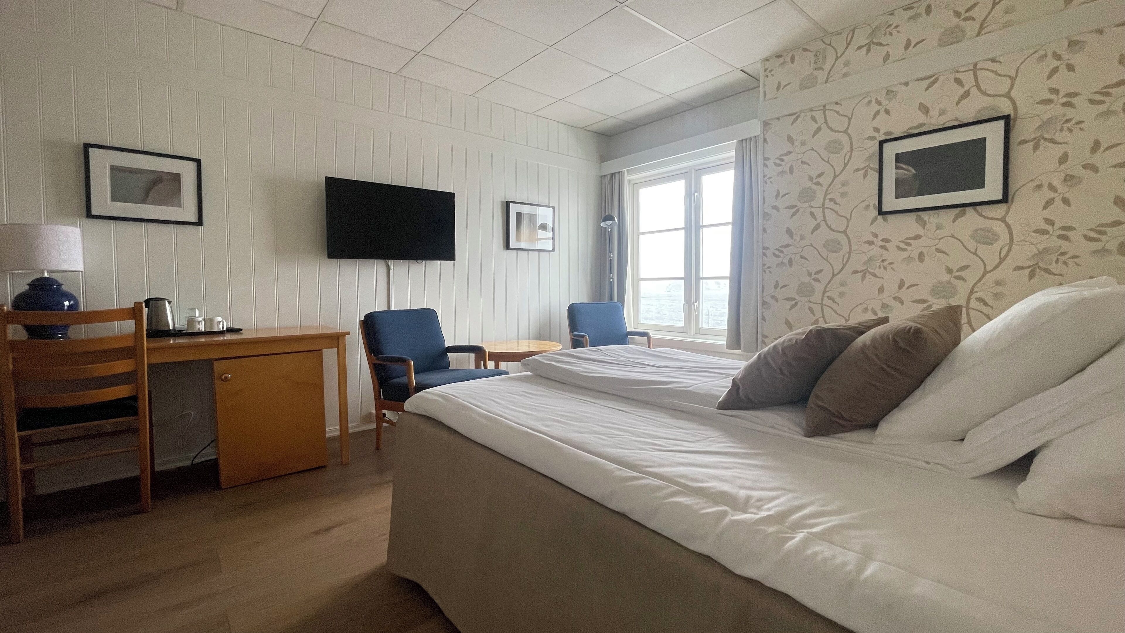 Hotellihuone, jossa on sänky, työpöytä, tuoleja ja televisio.