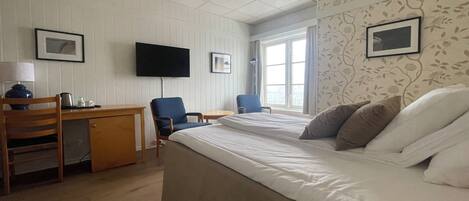 Hotellihuone, jossa on sänky, työpöytä, tuoleja ja televisio.