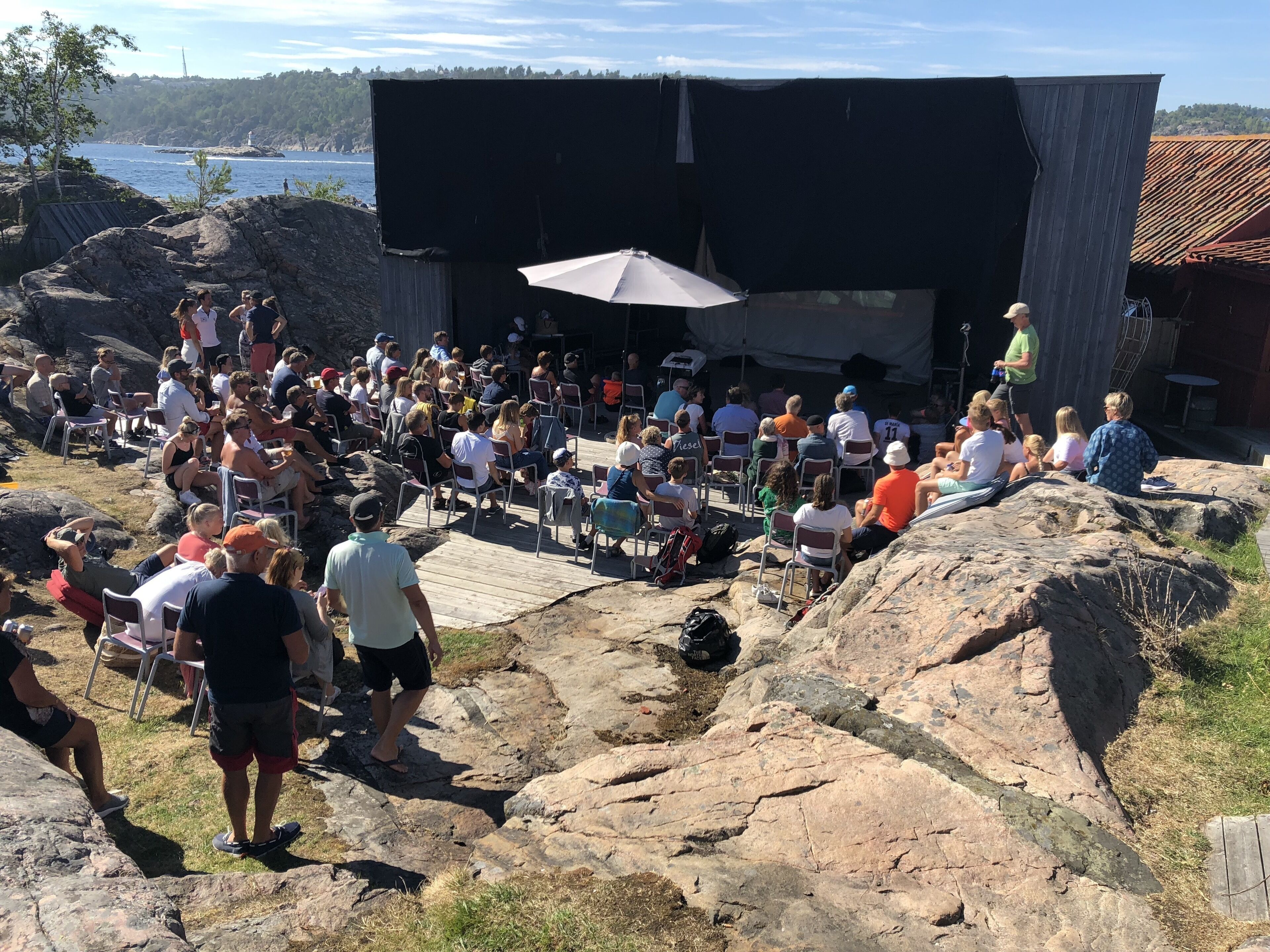 An outdoor amphitheater with a stage and audience seating on rocky terrain.