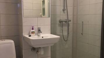Un baño con inodoro, lavabo con espejo y cabina de ducha con mampara de vidrio.