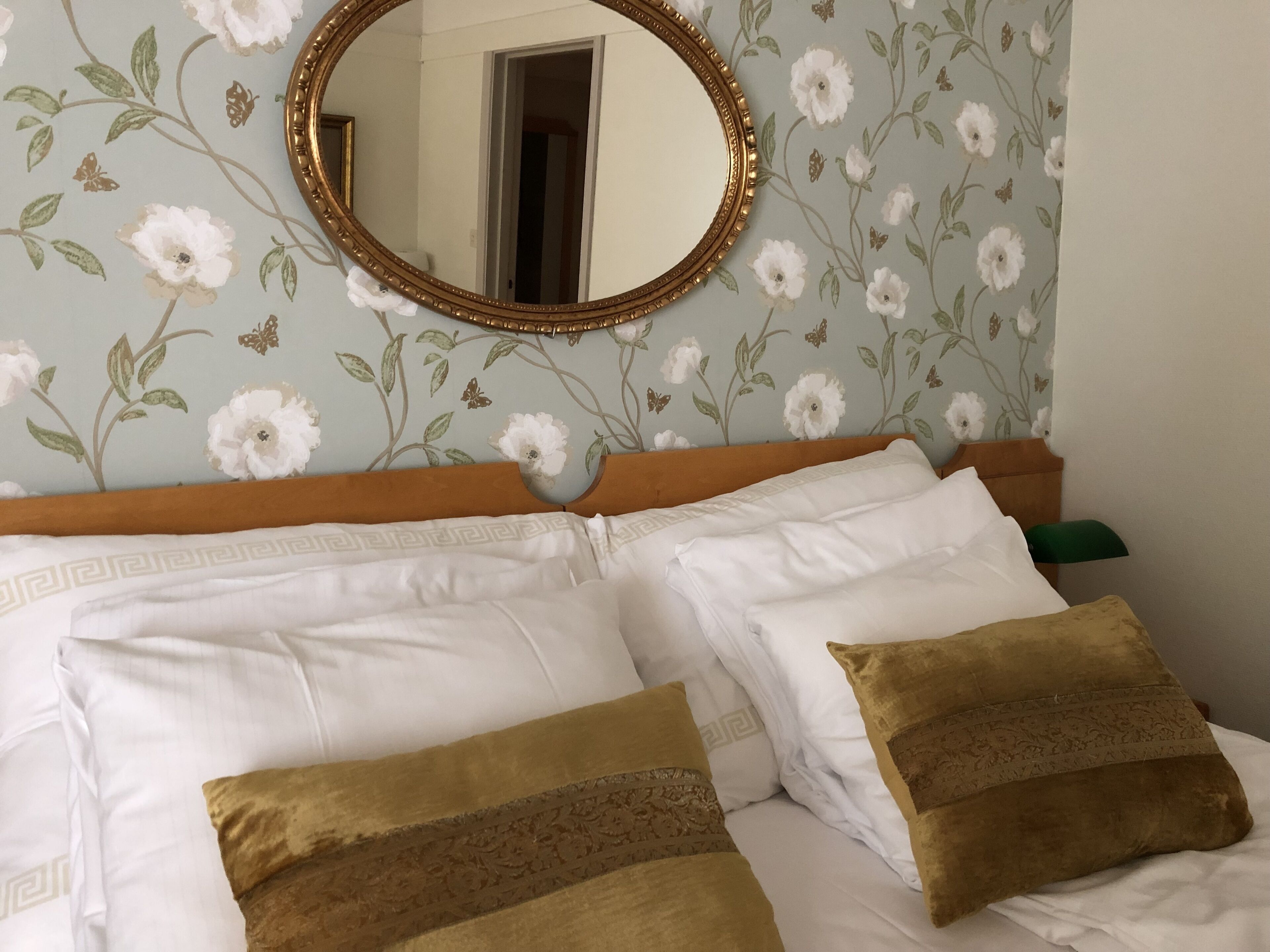 A bed with white and brown pillows, a wooden headboard, and a floral wallpaper.
