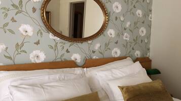 A bed with white and brown pillows, a wooden headboard, and a floral wallpaper.